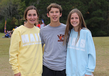 Two female students posing with a male student outside