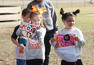 Three young students on the field holding up posters