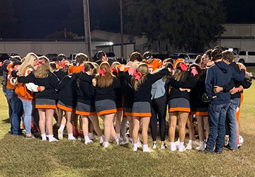 Football team and cheerleaders huddling together on a field